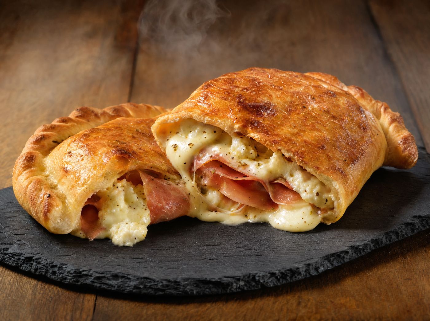 Golden baked calzone cut open, showing melted cheese and ham